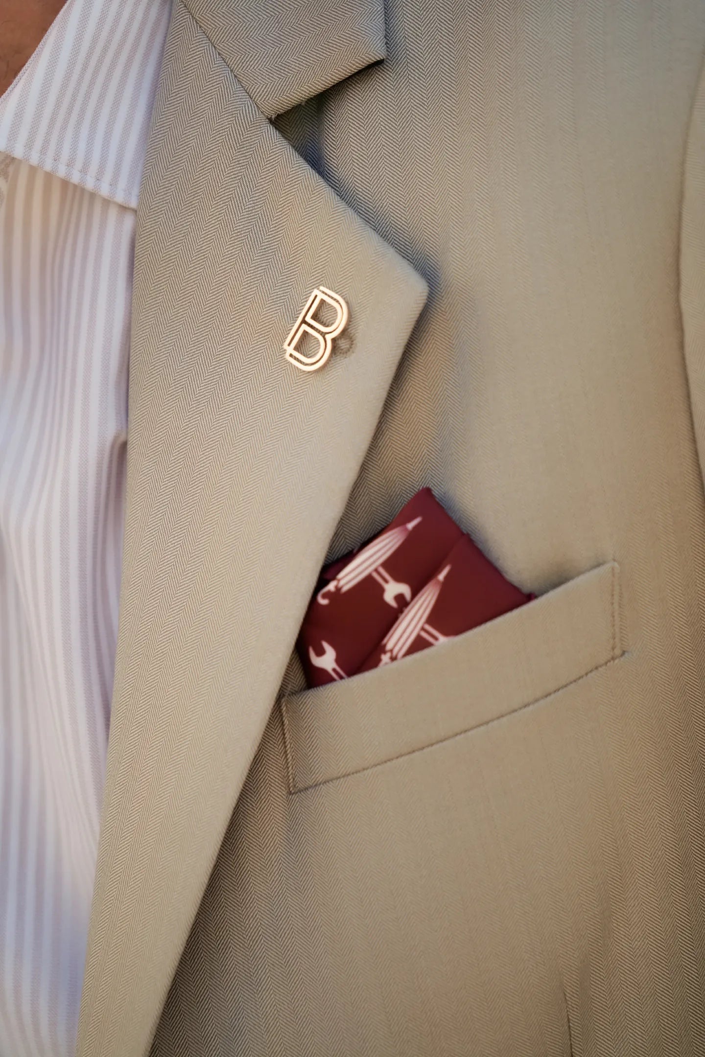 Close-up of the Brummell x DGR Limited Edition blazer showing the signature gold “B” lapel pin, herringbone Italian wool fabric, and burgundy DGR pocket square.